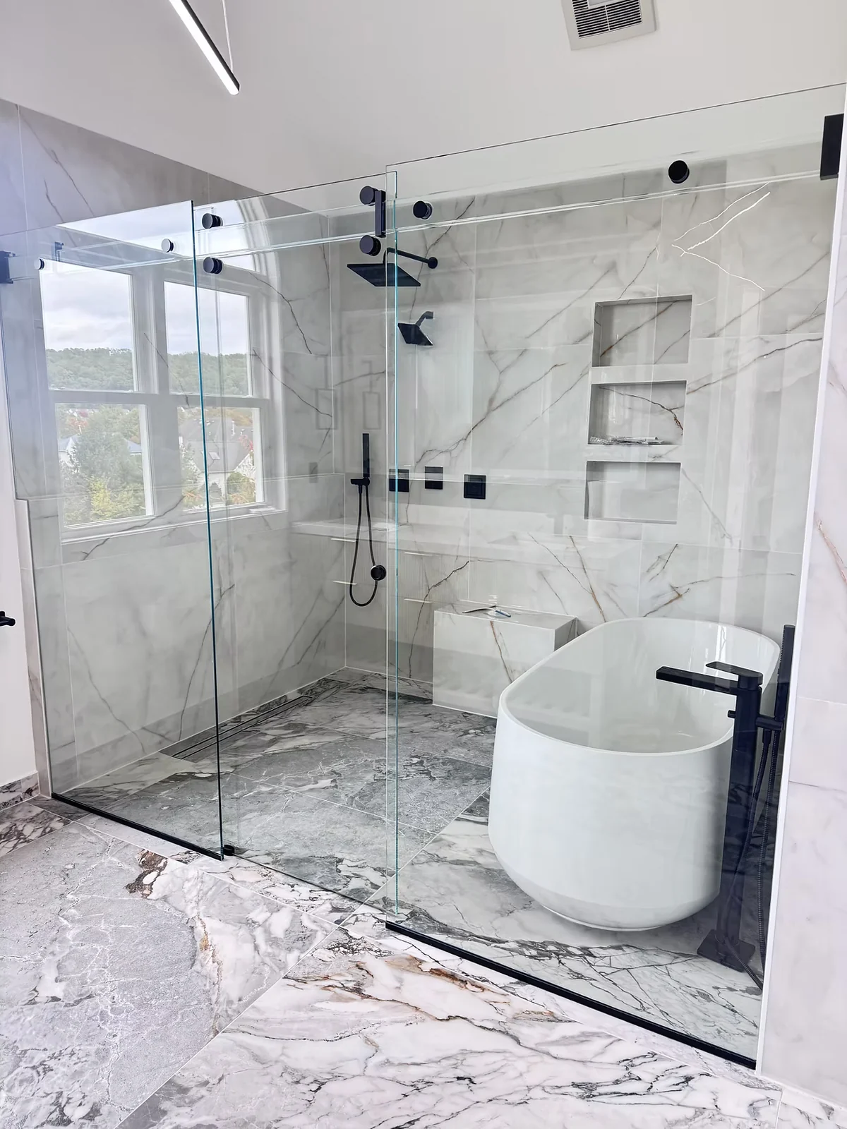 Titan Phantom sliding shower enclosure with a clear glass header and dark hardware beside a freestanding tub.