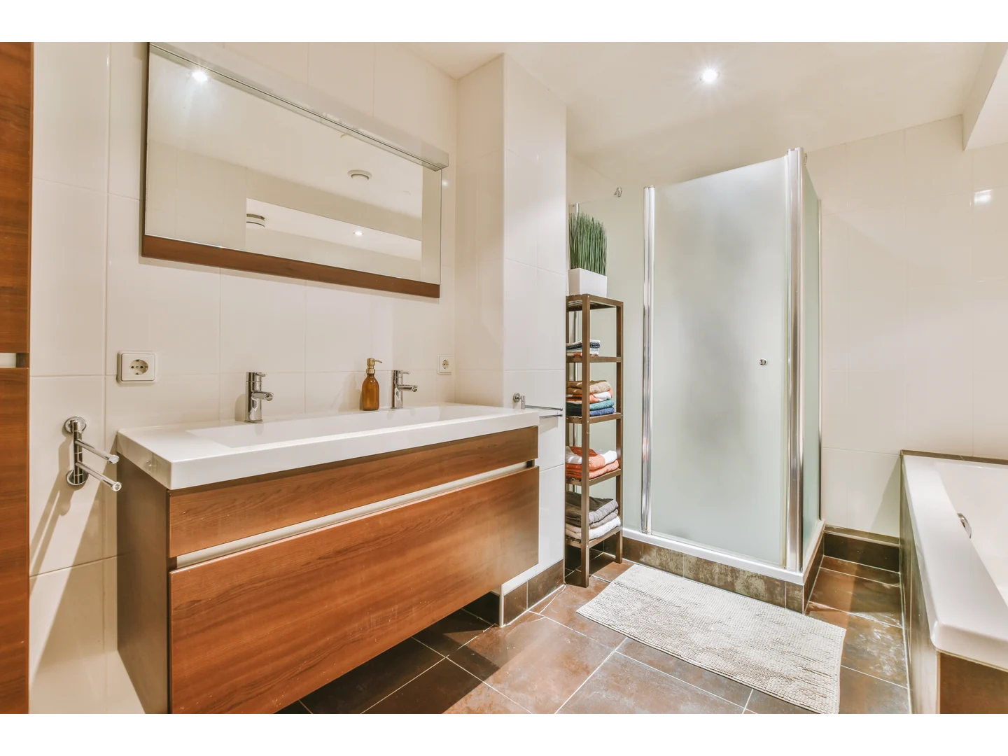 Frosted corner shower enclosure with silver-colored profiles beside a wood vanity and bathtub.