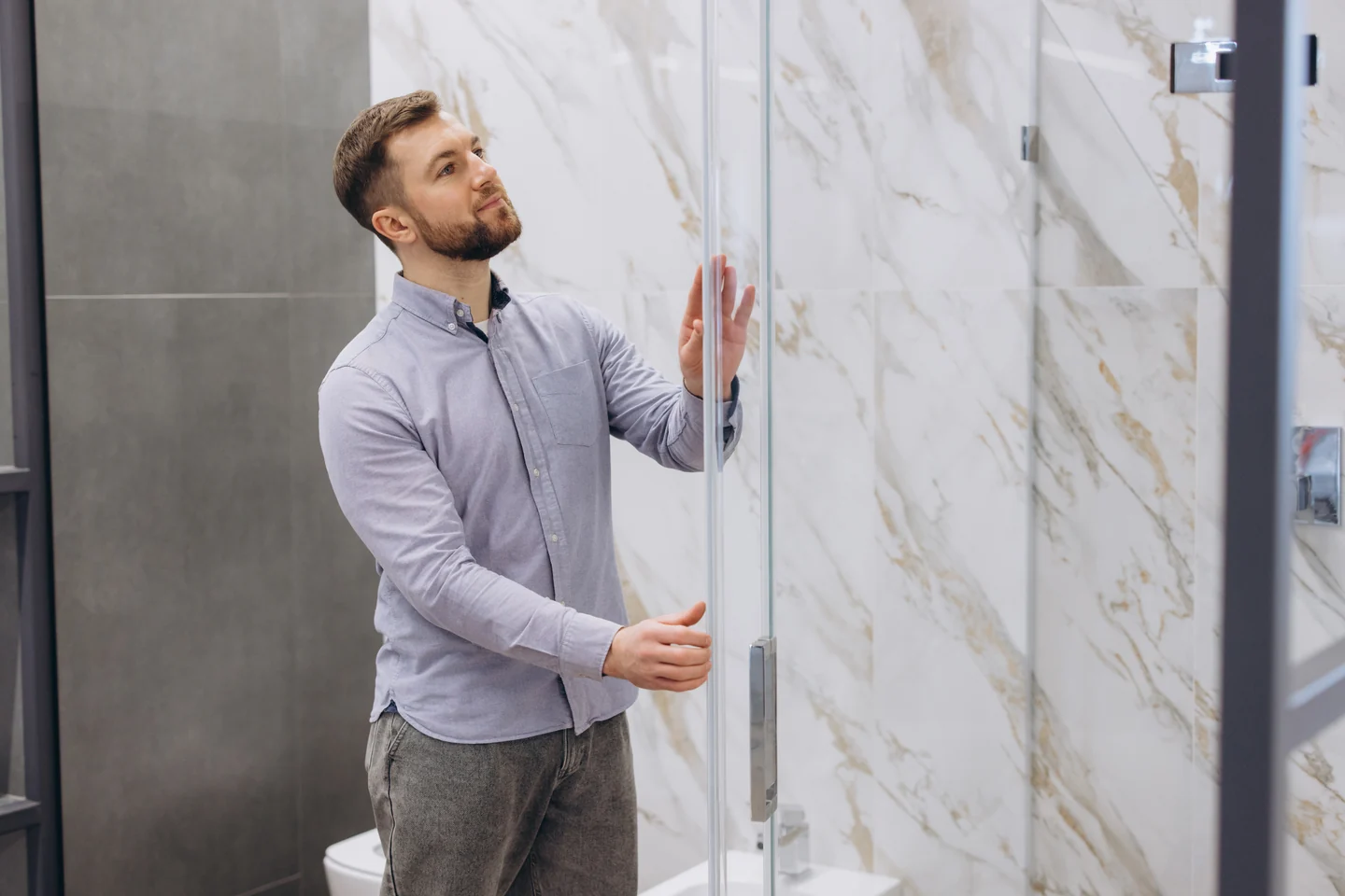 A person examining the glass and handle of a shower-door display.